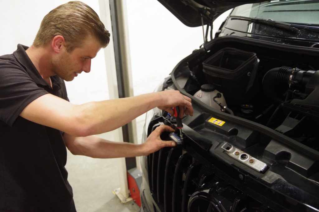 Monteur werkt met handgereedschap in de open motorruimte bij Autobedrijf van den Berg