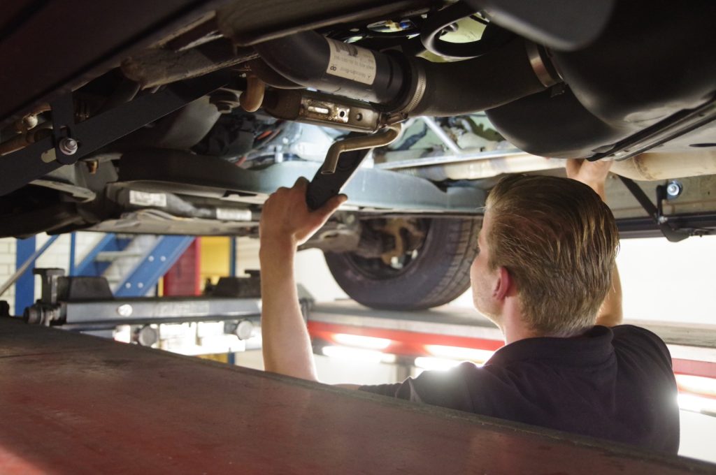 Monteur bekijkt met een inspectielamp onderdelen aan de onderzijde van een auto