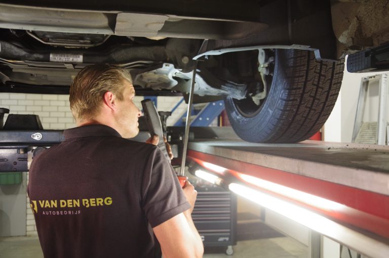 Monteur met inspectielamp onder een auto op de hefbrug bij Autobedrijf van den Berg